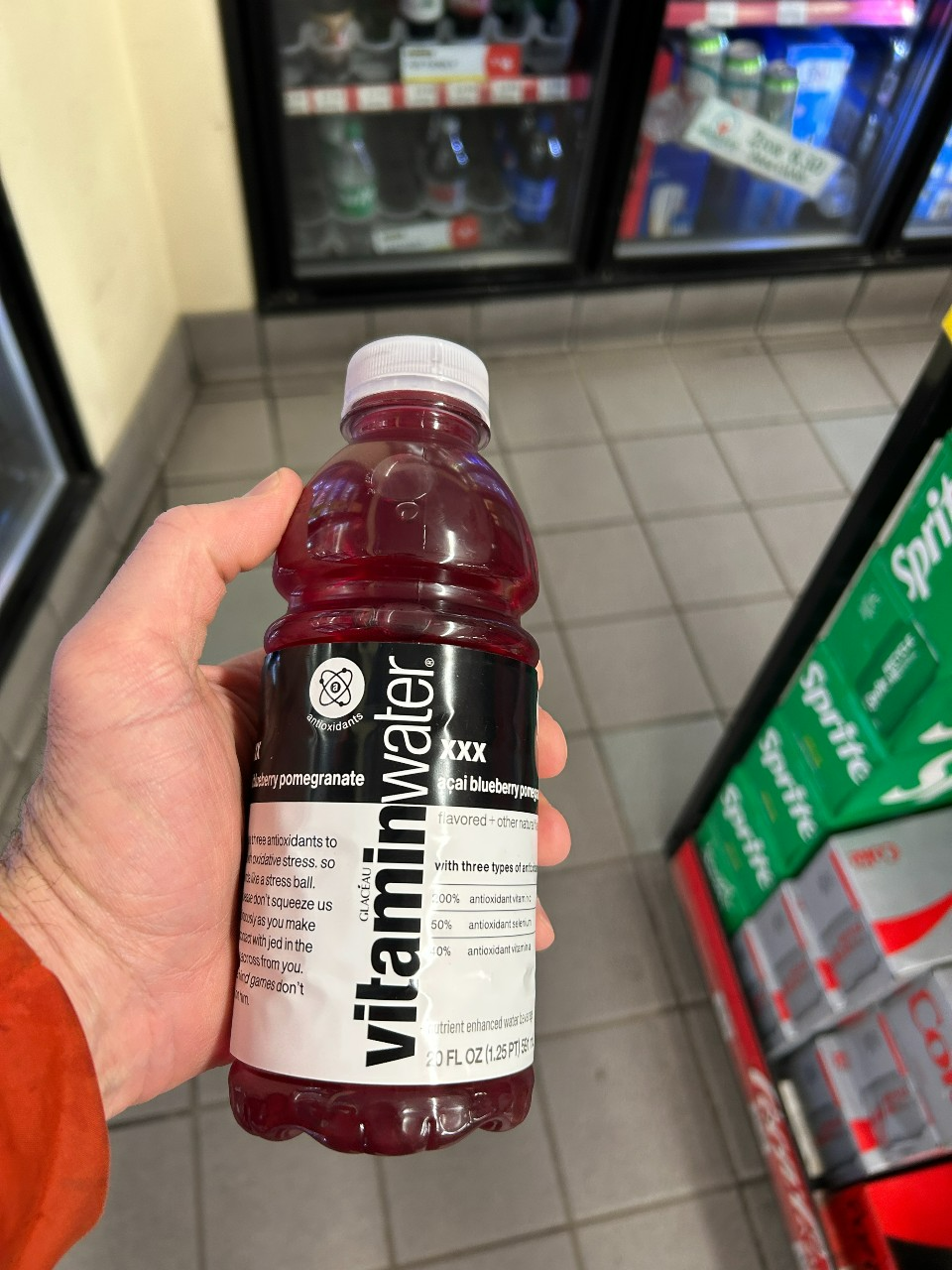 Hand holding a bottle of vitamin water in a convenience store cooler aisle